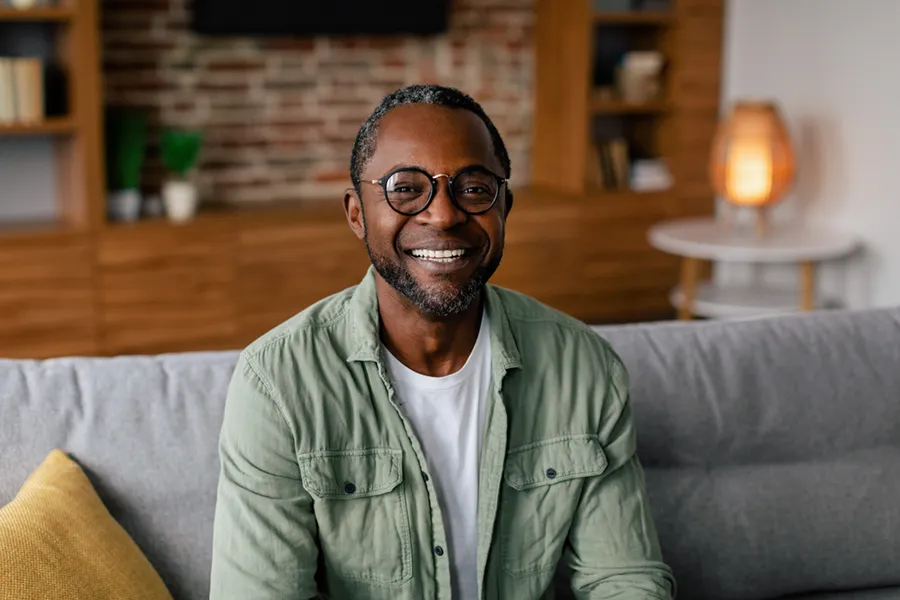 Andropause-Doctor A middle aged black man in a green button up shirt sits on his couch smiling, happy with his treatment for andropause and low testosterone from Better Life Carolinas of Mount Pleasant in Charleston Metro.