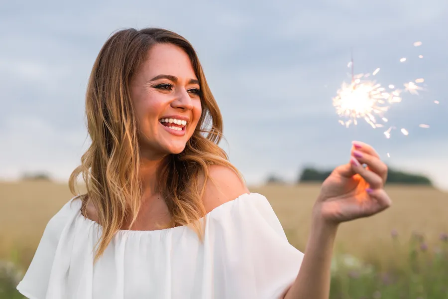 EMsella-for-Women-Clinic A cheerful young woman holding a lit sparkler in an open field at dusk satisfied with successful EMsella Pelvic Floor Strengthening treatment by Better Life Carolinas of Mount Pleasant in Charleston Metro.