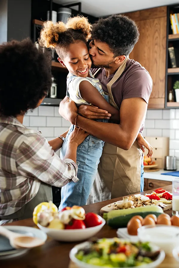 Gut-Health-Treatment A man holds his daughter and kisses her cheek as the family makes a healthy dinner in the kitchen. Get help for digestive issues and gut health from Better Life Carolinas of Mount Pleasant in Charleston Metro.