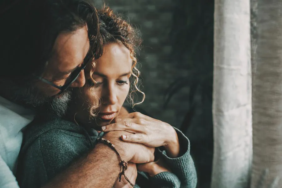 Neurodegenerative-Disorders-Therapy A man embraces a woman from behind in a dimly lit room, their somber expressions showing concerns about a neurodegenerative disease they will get treated by Better Life Carolinas of Mount Pleasant in Charleston Metro.