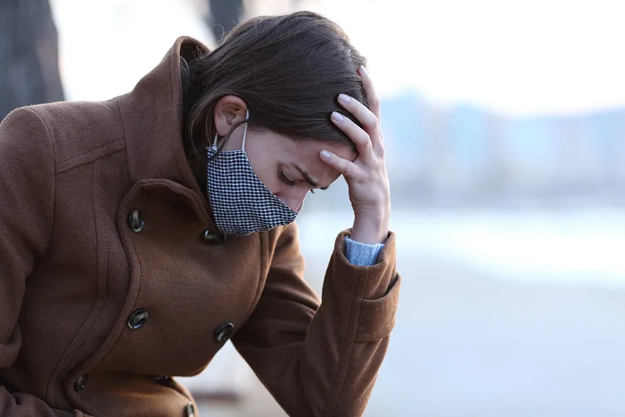 Post-Covid-Clinic A woman in a mask sits outside with her hand on her forehead in pain. Get long covid treatment from Better Life Carolinas of Mount Pleasant in Charleston Metro.