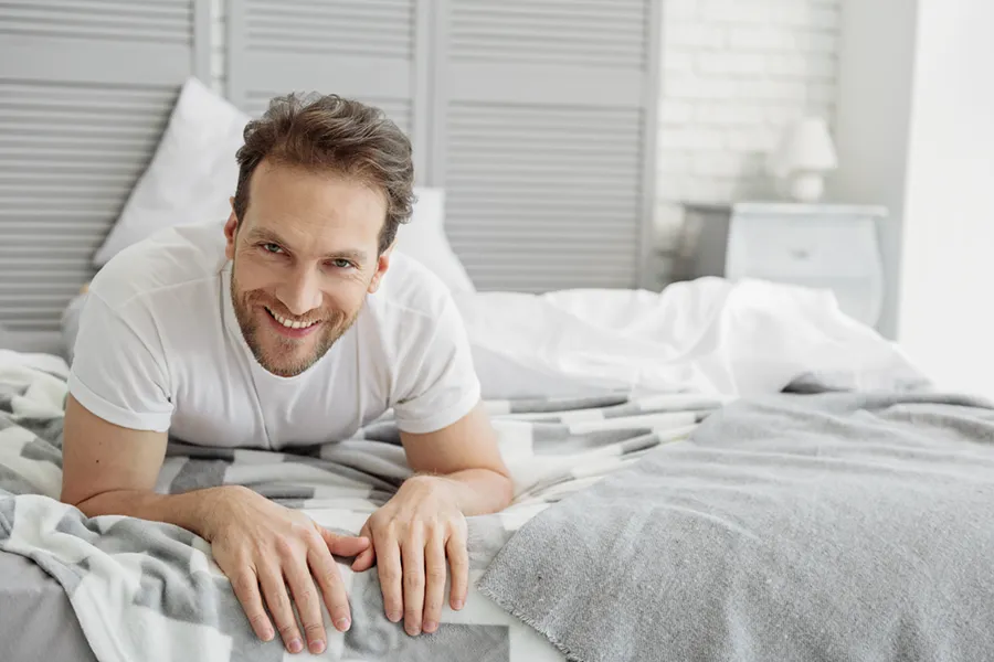 Sexual-Wellness-for-Men-Doctor A man in a t-shirt lies on his stomach in bed smiling, happy with his sexual wellness treatments from Better Life Carolinas of Mount Pleasant in Charleston Metro.
