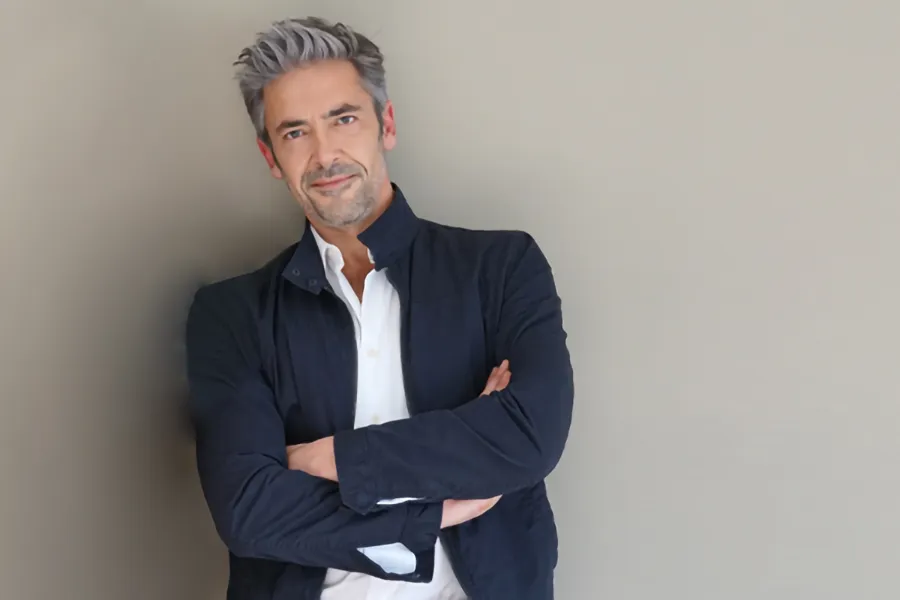 Testosterone-Low-T-Solutionsn-Clinic A middle-aged man in a white shirt and dark blue jacket leans against a gray wall smiling. Get testosterone for Low T from Better Life Carolinas of Mount Pleasant in Charleston Metro.